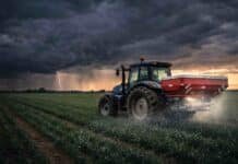 Se intensifica la crisis por la guerra: más del 50% de los alimentos podría verse afectado por la falta de fertilizantes Tractor fertilizador aplicando insumos en un cultivo bajo cielo tormentoso, reflejando el impacto de la disponibilidad de fertilizantes en la producción agrícola