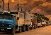 Refuerzan la seguridad y buscan destrabar el ingreso de camiones en Bahía Blanca tras días de parálisis portuari Fila de camiones cerealeros en acceso al puerto de Bahía Blanca bajo cielo de atardecer con tonos naranja, en un contexto de reactivación de la logística agroindustrial.
