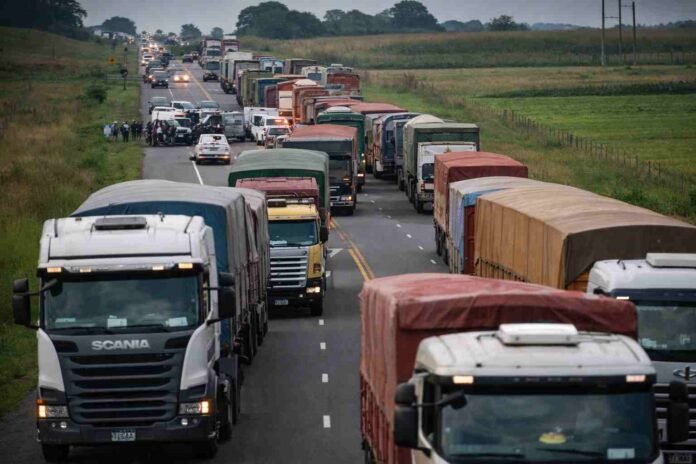 camiones-ruta-colapsada-cosecha-logistica-agro-santa-fe-ruralnet Larga fila de camiones detenidos sobre una ruta rural durante la cosecha, con congestión logística y tránsito saturado en una zona productiva de Santa Fe.