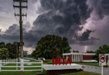 El Gobierno pone en venta hasta 42.000 hectáreas del INTA y crece la tensión en el agro Entrada del INTA con cartel institucional bajo cielo oscuro de tormenta, nubes cumulonimbus y relámpago en el fondo, ambiente lluvioso y amenazante en un predio rural argentino.