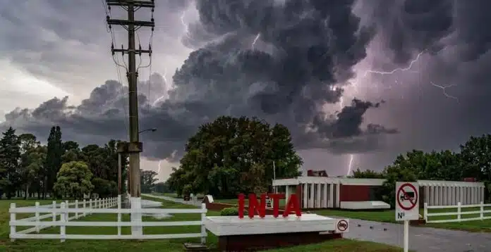 inta-tormenta-cielo-amenazante-1200px-ruralnet Entrada del INTA con cartel institucional bajo cielo oscuro de tormenta, nubes cumulonimbus y relámpago en el fondo, ambiente lluvioso y amenazante en un predio rural argentino.