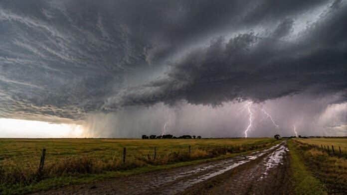 Tormenta intensa con relámpagos y lluvia sobre campo agrícola y camino rural inundado