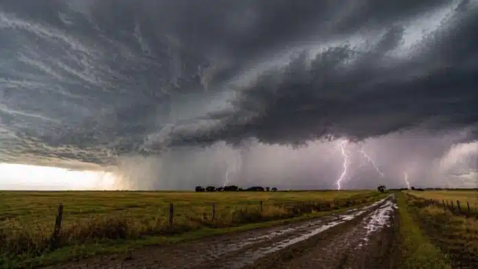 Tormenta intensa con relámpagos y lluvia sobre campo agrícola y camino rural inundado