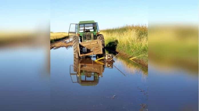 tractor-encajado-camino-rural-inundado-crisis-hidrica-9-de-julio-ruralnet Tractor detenido en un camino rural completamente inundado, con agua cubriendo la traza y reflejando la crisis hídrica que afecta a zonas productivas de Buenos Aires.