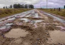 Más de 20 proyectos clave para el campo siguen frenados en la Legislatura bonaerense Camino rural en muy mal estado con barro, pozos profundos y charcos de agua, rodeado de campos y alambrados bajo un cielo nublado.