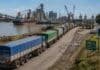 Santa Fe defiende el fideicomiso portuario: “A nadie le gusta pagar, pero las rutas no aguantan más Fila de camiones cerealeros avanzando hacia una terminal portuaria argentina junto al río, con barcos, grúas y plantas industriales visibles en el puerto.