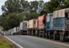 La Sociedad Rural de Rosario rechaza el fideicomiso vial de Santa Fe: “Ya pagamos U$S 103 por tonelada de soja en retenciones” Larga fila de camiones cerealeros circulando por una ruta argentina rodeada de árboles y paisaje rural.