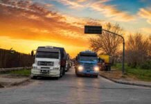 Santa Fe propone un fideicomiso de U$S 1,5 por tonelada para rutas del Gran Rosario y aclara que deben pagarlo las exportadoras Fila de camiones cargados con granos esperando ingresar a terminales portuarias del Gran Rosario bajo un cielo de atardecer.