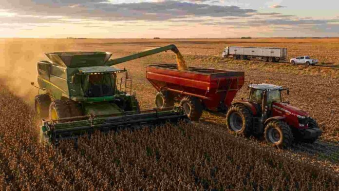 Cosechadora John Deere descargando soja sobre una tolva Akron tirada por un tractor Massey Ferguson durante la cosecha de soja en la región pampeana argentina al atardecer