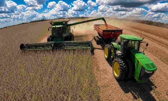 Cosechadora y tractor descargando soja en una tolva durante la cosecha en un campo argentino bajo grandes nubes de tormenta y cielo parcialmente cubierto