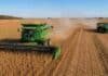 La cosecha de soja va 15% atrasada y los productores guardan el grano: la comercialización, en mínimos históricos Cosechadora trabajando sobre un lote de soja madura en la región agrícola argentina, con tractor y tolva autodescargable en plena cosecha bajo cielo despejado.