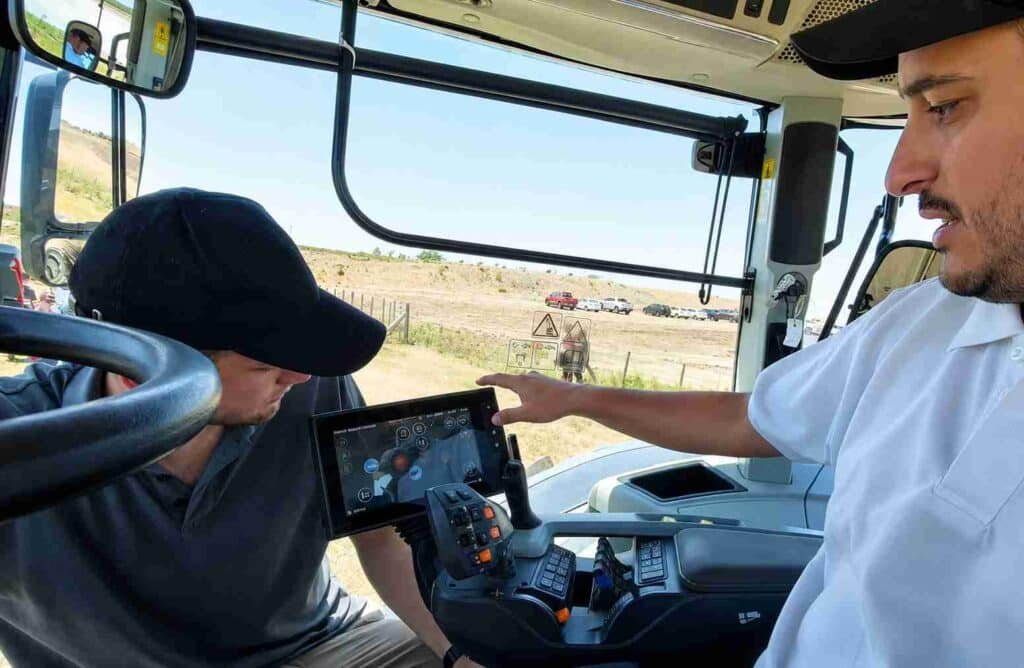 Interior de la cabina de una maquinaria agrícola durante una experiencia de manejo, con un instructor señalando la pantalla de control al operador.