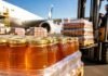 Las exportaciones de miel argentina batieron el récord de los últimos 20 años: U$S 74 millones y casi 30.000 toneladas en el primer trimestre Frascos de miel listos para exportación junto a un avión de carga y pallets logísticos en una terminal aeroportuaria.