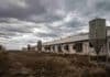La mayor avícola del país faenó un tercio de lo que podía y sus productores no saben si van a cobrar Galpones avícolas vacíos y silos abandonados en una zona rural de Argentina bajo un cielo nublado y ambiente desolado