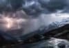 Alerta meteorológica en la Patagonia: lluvias persistentes y posibles nevadas en zona cordillerana Tormenta eléctrica sobre la cordillera de los Andes en la Patagonia con relámpagos, lluvia intensa y nieve en cumbres, camino de montaña mojado en primer plano.
