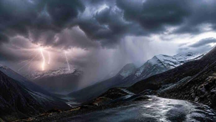 Tormenta eléctrica sobre la cordillera de los Andes en la Patagonia con relámpagos, lluvia intensa y nieve en cumbres, camino de montaña mojado en primer plano.