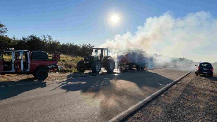 Tractor y acoplado envueltos en humo sobre una ruta rural mientras bomberos y policía trabajan en un operativo de emergencia.
