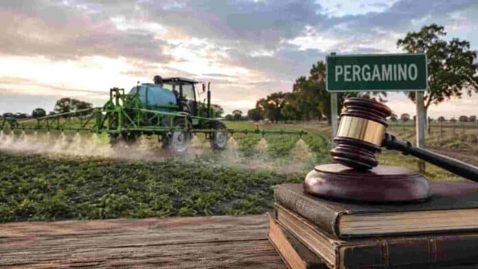 Pulverizadora agrícola trabajando en un campo de Pergamino junto a un martillo judicial como referencia al juicio por contaminación con agroquímicos.