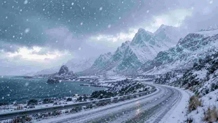 Ruta de montaña cubierta de nieve durante una nevada intensa, con cordillera, viento fuerte y condiciones invernales severas.