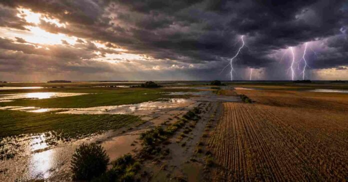 Vista aérea de campos agrícolas inundados en la región pampeana argentina bajo una tormenta severa, con relámpagos sobre el horizonte, nubes oscuras y cultivos parcialmente cubiertos por agua al atardecer.