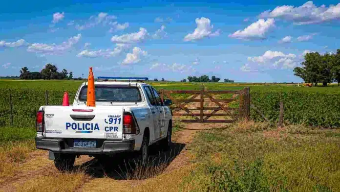 control-policial-rural-campo-tranquera-ruralnet Camioneta policial rural estacionada junto a una tranquera de madera en un campo agrícola, bajo cielo despejado con nubes