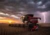 Con el norte y centro ya finalizados, la cosecha de soja avanza sobre el sur con rindes rezagados Cosechadora Massey Ferguson trabajando en la cosecha de soja en un campo de la zona núcleo al atardecer, con nubes de tormenta y un relámpago de fondo.