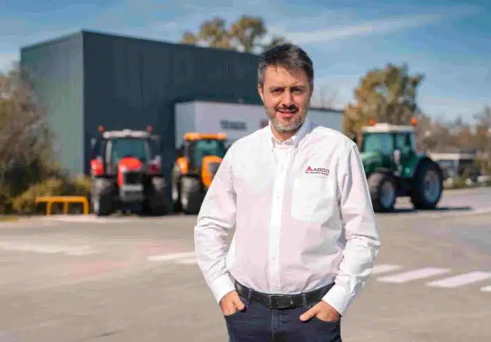 emiliano-ferrari-agco-tractores-ruralnet Emiliano Ferrari, representante de AGCO Argentina, posando frente a instalaciones de la compañía con tractores agrícolas al fondo en un entorno corporativo vinculado al sector agropecuario.