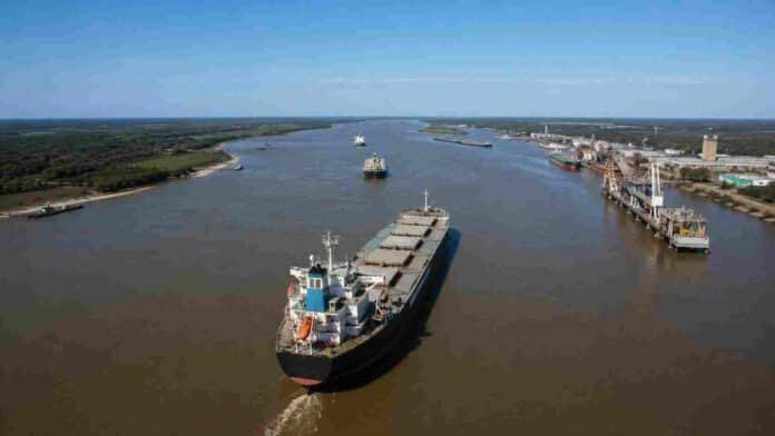 hidrovia-parana-paraguay-concesion-dragado-ruralnet Buque de carga navegando por la Hidrovía Paraná-Paraguay junto a terminales portuarias y plantas agroexportadoras, representando el transporte de granos y el comercio exterior argentino.
