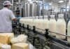 El Gobierno eliminó un registro que regía la lechería argentina desde 2006 Planta industrial láctea con botellas de leche en línea de producción, operario controlando maquinaria y productos como queso y ricota en primer plano.