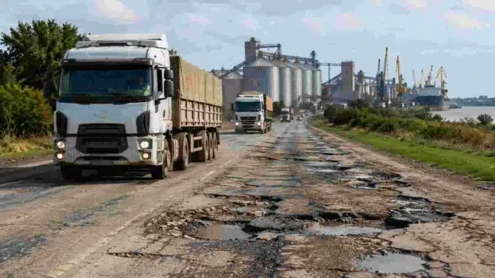 rutas-deterioradas-gran-rosario-logistica-agro-ruralnet Camiones transportando granos sobre una ruta nacional deteriorada en Santa Fe, con baches y asfalto dañado camino a los puertos agroexportadores del Gran Rosario.