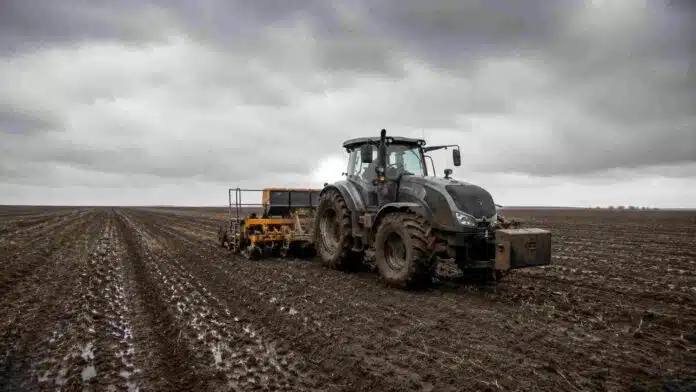 Tractor Valtra HiTech con sembradora de granos finos trabajando sobre un lote húmedo de la región pampeana, con suelo oscuro recién sembrado y cielo nublado de invierno.