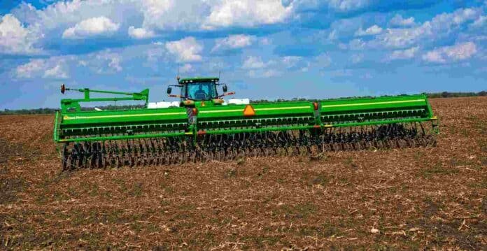 siembra-de-trigo-en-campo-agricola Sembradora de granos finos trabajando en un campo agrícola con rastrojo, bajo un cielo despejado con nubes, durante una jornada de siembra de trigo.