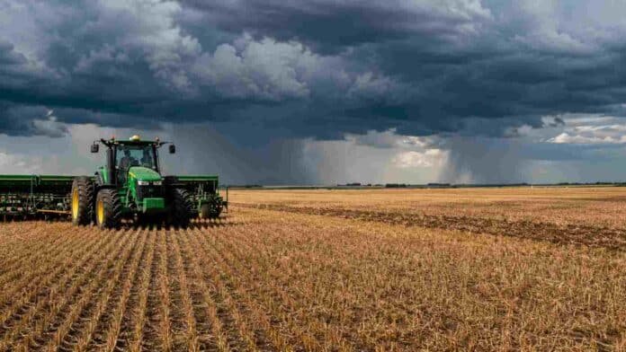 Tractor con sembradora trabajando sobre rastrojo en un campo agrícola argentino, bajo un cielo nublado con tormentas y cortinas de lluvia en el horizonte