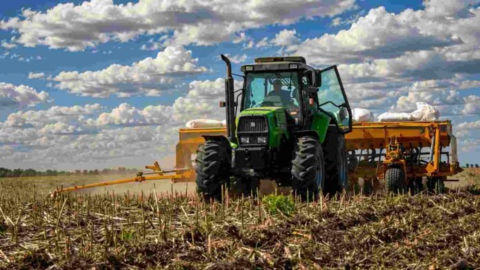 Tractor verde con sembradora trabajando sobre rastrojo en un lote agrícola argentino, bajo cielo con nubes y colores vívidos durante la siembra de trigo.