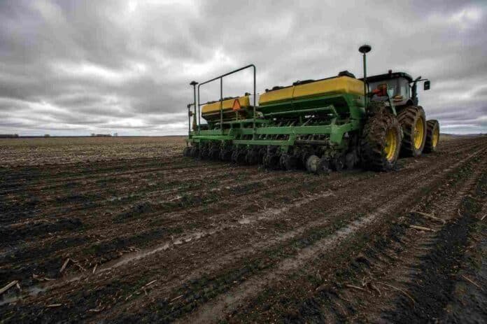 siembra-trigo-suelo-humedo-llanura-pampeana-ruralnet Sembradora de trigo trabajando sobre suelo oscuro y húmedo en la llanura pampeana argentina, con surcos cerrados, barro en las ruedas, rastrojos del cultivo anterior y cielo nublado de invierno.