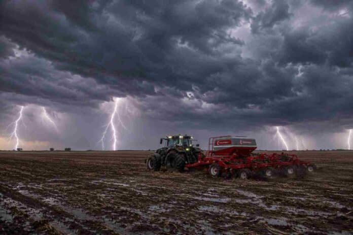 Tractor con sembradora de granos finos trabajando sobre rastrojo de soja en la Pampa Húmeda, bajo un cielo de tormenta con relámpagos, lluvia y suelo mojado.