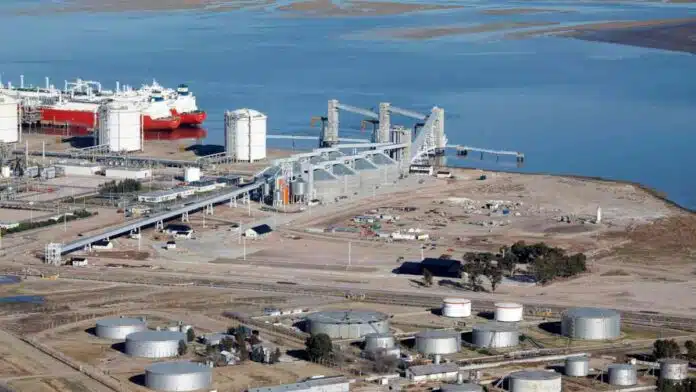 terminal-portuaria-exportacion-industrial Vista aérea de una terminal portuaria e industrial junto a un río, con silos, tanques de almacenamiento y buques de carga destinados a exportación.