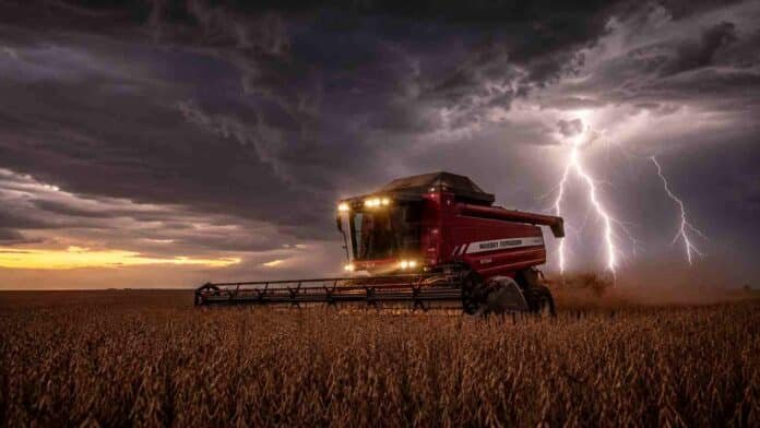 Cosechadora Massey Ferguson con luces encendidas trabajando en un lote de soja R7 a punto de cosecha, bajo un cielo de tormenta con relámpagos en la región pampeana argentina.