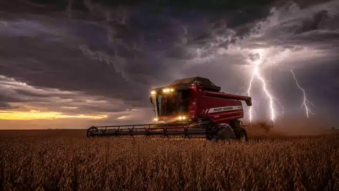 Cosechadora Massey Ferguson con luces encendidas trabajando en un lote de soja R7 a punto de cosecha, bajo un cielo de tormenta con relámpagos en la región pampeana argentina.