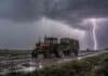 Alerta por tormentas fuertes este jueves: el SMN prevé hasta 70 mm en seis provincias Tractor Zanello antiguo con cabina tirando un acoplado playo con rollos de alfalfa bajo una tormenta con lluvia y relámpagos en un camino rural embarrado