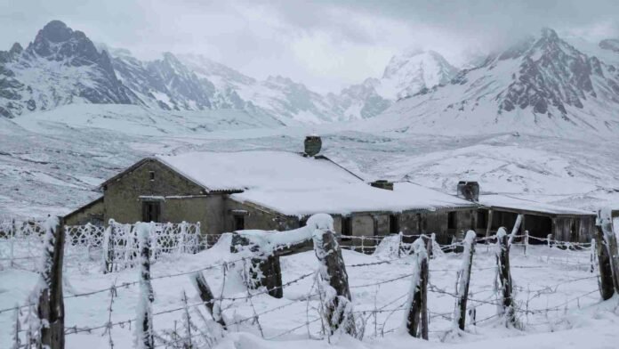 estancia-patagonica-nevada-cordillera-ruralnet Casco de estancia patagónica cubierto de nieve, con alambrados nevados y la cordillera de fondo bajo un cielo encapotado.