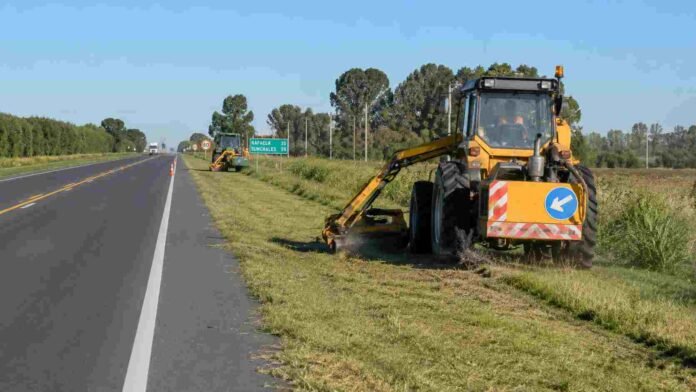mantenimiento-banquinas-ruta-argentina-ruralnet Maquinaria vial realizando tareas de mantenimiento y corte de pasto en la banquina de una ruta nacional argentina, con tránsito y campos rurales de fondo.