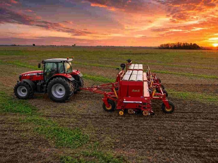 Tractor Massey Ferguson 6700 con sembradora trabajando en un campo durante el atardecer.