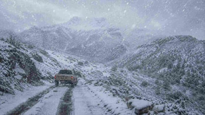 Camioneta 4x4 circula por un camino de montaña cubierto de nieve durante una intensa nevada en la cordillera patagónica argentina.