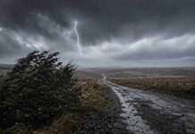 Alerta naranja por lluvias, nieve y ráfagas de hasta 110 km/h: las zonas bajo alerta Camino rural bajo una tormenta intensa con lluvia, viento fuerte y un relámpago sobre un paisaje abierto.