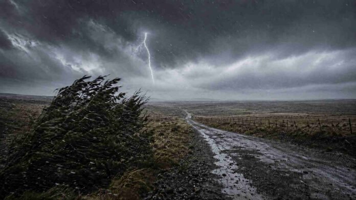 Camino rural bajo una tormenta intensa con lluvia, viento fuerte y un relámpago sobre un paisaje abierto.