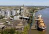 Molinos Agro y ACA invertirán US$ 500 millones en una mega planta de soja en Timbúes Planta agroexportadora con silos, camiones y buque cargando granos en un puerto sobre el río Paraná.