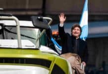 El agro espera a Milei: la inauguración cambia de día y formato Un mandatario saluda junto a maquinaria agrícola y una bandera argentina durante un acto en la Exposición Rural de Palermo.