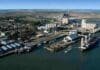 El 65% de los granos argentinos se produce a menos de 300 km de los principales puertos Vista aérea de un puerto industrial con silos, terminales de carga, depósitos y buques amarrados.