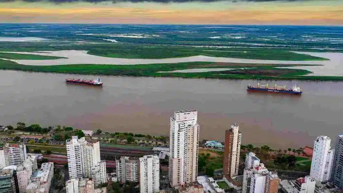 Vista aérea de la ciudad de Rosario y el río Paraná, con buques navegando frente a la costa y las islas del delta al fondo.